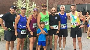 A group of eight people, seven adults and one child, stand together in running attire with Kilomaîtres LaSalle race numbers, posing for a photo outdoors. A building and plants are visible in the background.