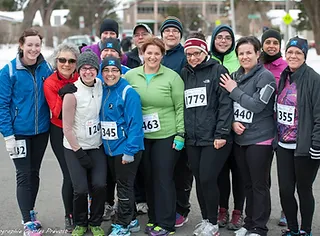 A group of runners, wearing numbered race bibs and dressed in cold-weather athletic gear, stand together for a group photo outdoors. This dedicated team also enjoys engaging in marche rapide to diversify their training.