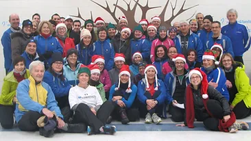 A group of people wearing winter clothing and Santa hats, ready for some festive marche rapide, pose together in front of a wall mural depicting a tree.