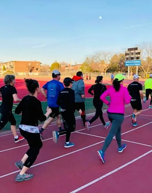 A group of people is engaged in marche rapide on a track during daytime under clear skies. They are all dressed in athletic attire, moving briskly with determined expressions.