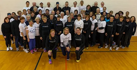 A large group of smiling people in athletic attire, proudly representing Kilomaîtres LaSalle, stand and sit in a gymnasium for a group photo.