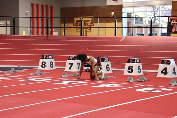 An athlete from the club d’athlétisme prepares to start a sprint race on a red indoor track, positioned in lane 7.