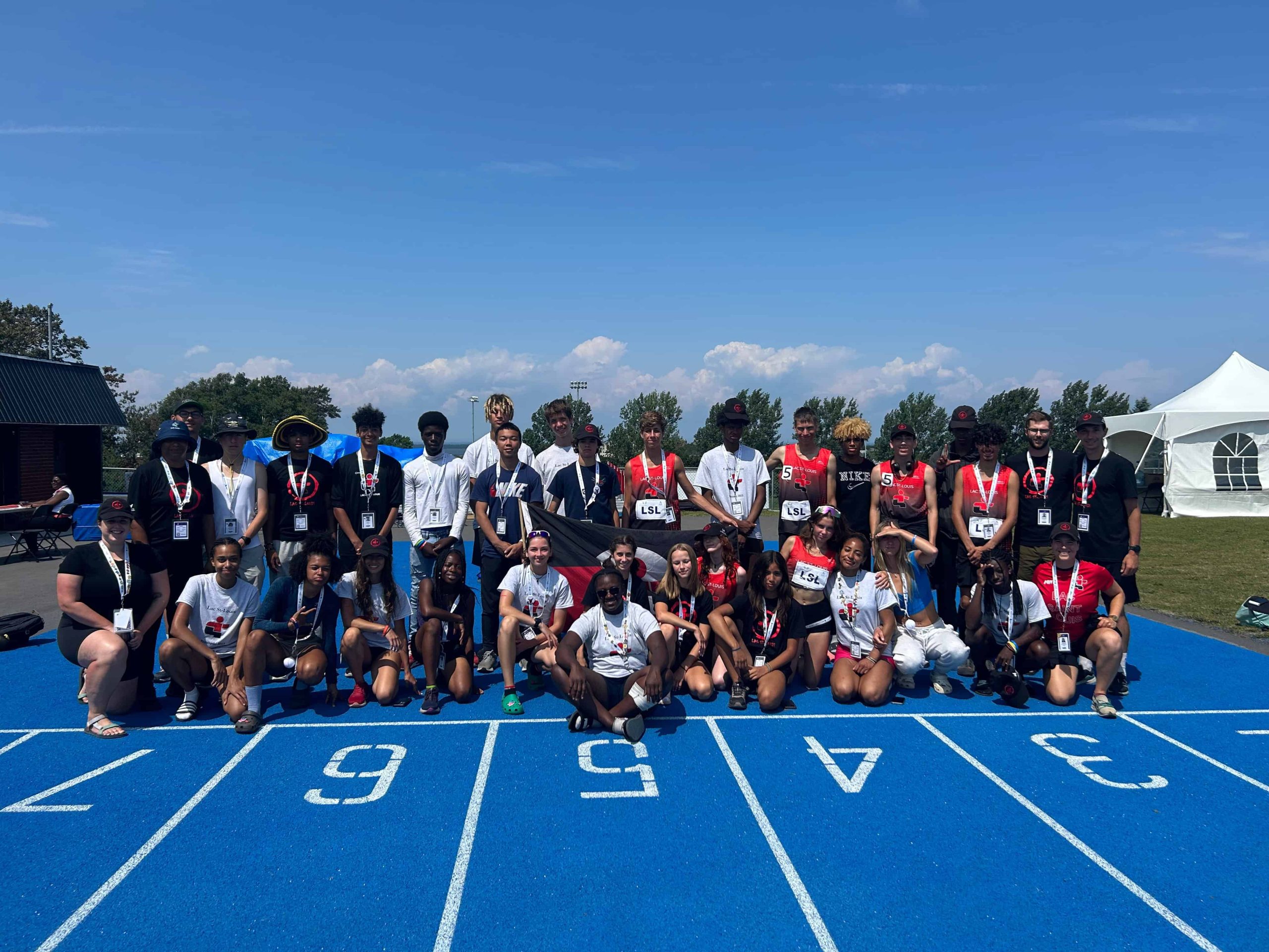 A group of people dressed in sports attire posing together on a blue running track, beneath a clear sky with tents in the background, proudly representing Kilomaîtres LaSalle.